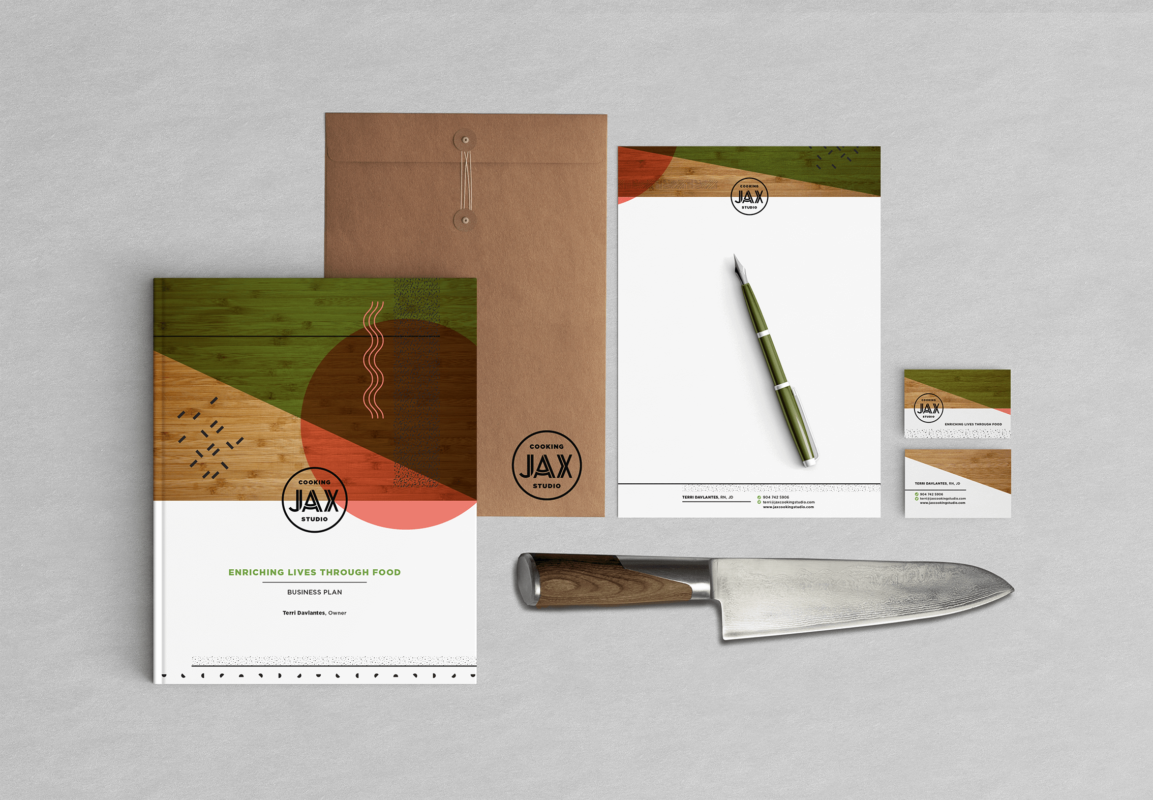 A notebook, letterhead, envelope, and business cards illustrating the JAX Cooking Studio business design system. A green pen and chef's knife provide extra setting.